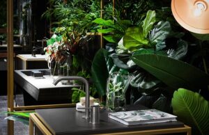 Luxurious bathroom with lush green plants, sleek modern fixtures, and ambient lighting. Elegant decor includes glass vases and a stylish magazine on the counter.