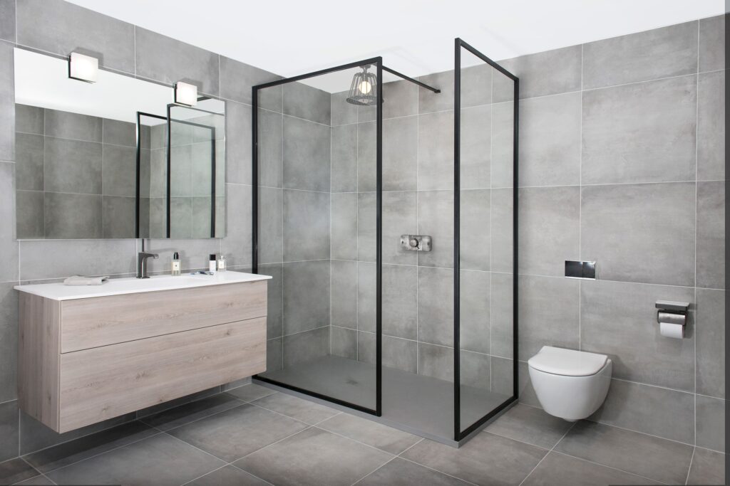 Modern bathroom with gray tiles, sleek floating vanity, large mirror, glass-enclosed shower, and toilet. Minimalist design ensures clean, functional space.