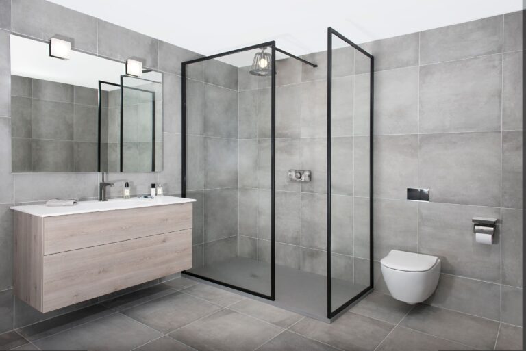 Modern bathroom with gray tiles, sleek floating vanity, large mirror, glass-enclosed shower, and toilet. Minimalist design ensures clean, functional space.