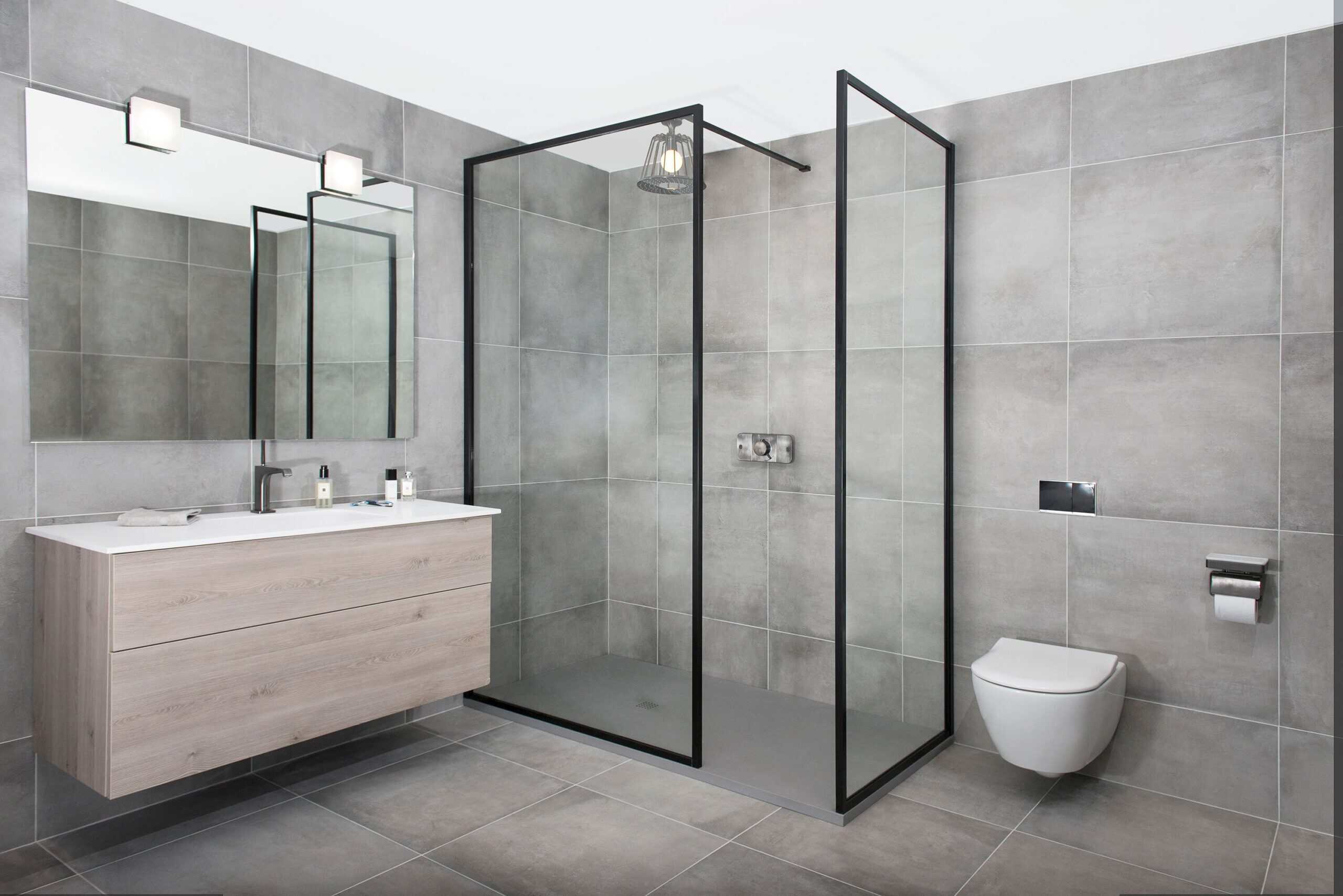 Modern bathroom with gray tiles, sleek floating vanity, large mirror, glass-enclosed shower, and toilet. Minimalist design ensures clean, functional space.