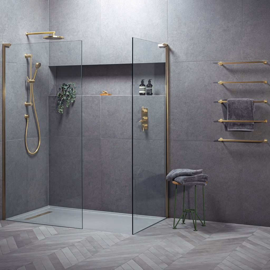 Modern bathroom with gray tiles, gold fixtures, and glass shower. Towel rack and green stool with folded towels add a sleek, minimalist touch.