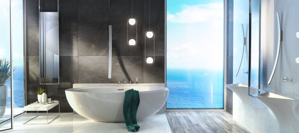 Modern bathroom with freestanding bathtub, large windows showing ocean view, and sleek fixtures. Minimalist design with white and gray tones and ambient lighting.