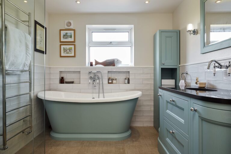 Stylish bathroom with a standalone tub, teal cabinetry, and decorative wall art, featuring bright natural light from an open window.