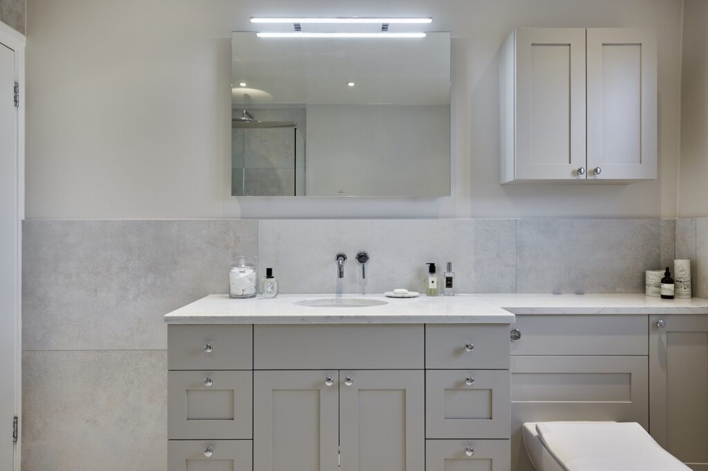 Modern bathroom with gray cabinets, large mirror, and sleek countertop. Neutral tones create a clean, minimalist design. Towel and toiletries neatly arranged.