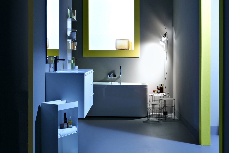 A modern, minimalist bathroom with a bathtub, wall-mounted cabinet, shelves, ambient lighting, and a round side table; blue walls and yellow accents.