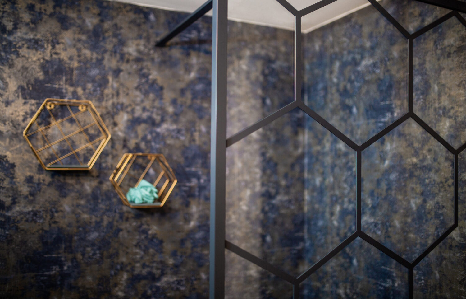 Geometric shelves with decor against a textured blue wall, adjacent to a glass partition with a hexagonal design. Modern, stylish interior look.