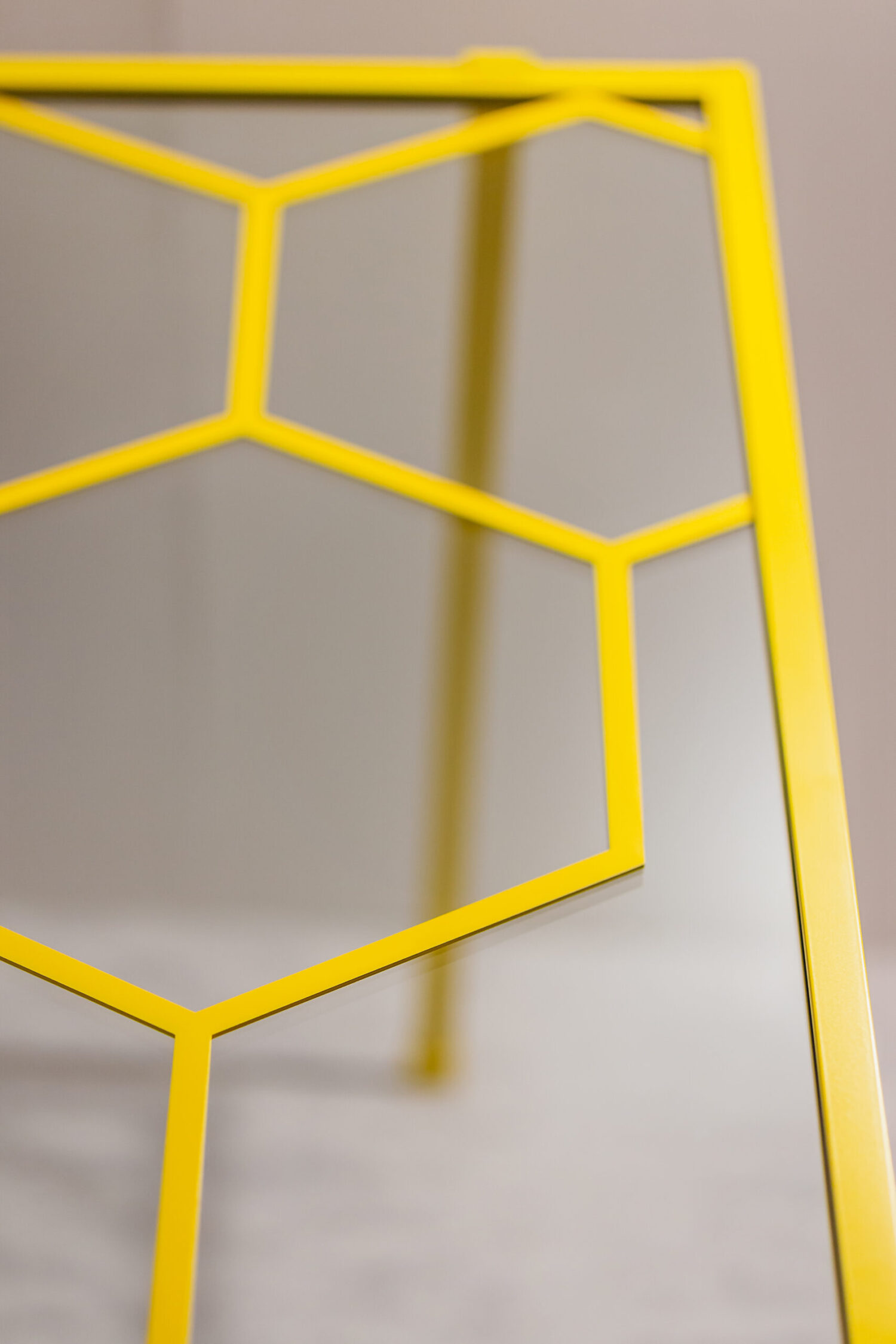 A close-up of a table with a yellow honeycomb-shaped metal frame and glass top. The background is a neutral, soft focus.