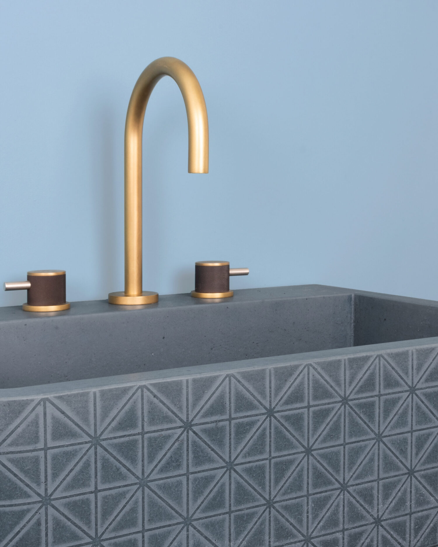 Modern bathroom sink with a geometric-patterned gray basin, featuring a sleek, gold-colored faucet against a light blue wall. Minimalistic and elegant design.