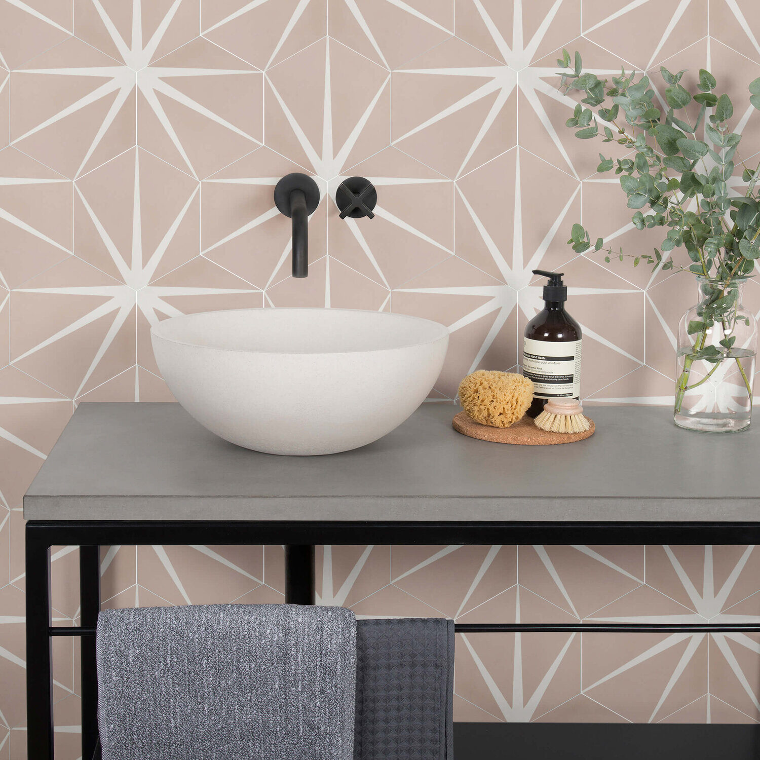 Modern bathroom sink setup with geometric-patterned wallpaper, round bowl basin, black fixtures, and decorative items like a soap bottle, sponge, and towel.