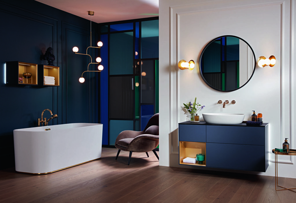 Modern bathroom with a white freestanding tub, navy blue vanity, circular mirror, and stylish lighting. Vibrant accents decorate the elegant space.