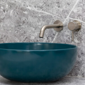 A modern bathroom with a sleek, round teal basin and stainless steel wall-mounted faucet against a grey marble background. Stylish and minimalist design.