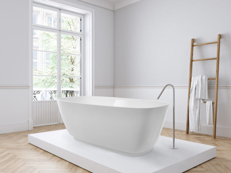Minimalist bathroom with freestanding bathtub on white platform, near a large window. Wooden ladder with towels against the wall, parquet flooring.