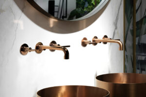 Modern bathroom design featuring elegant bronze faucets and matching sinks against a marble wall with a large round mirror.