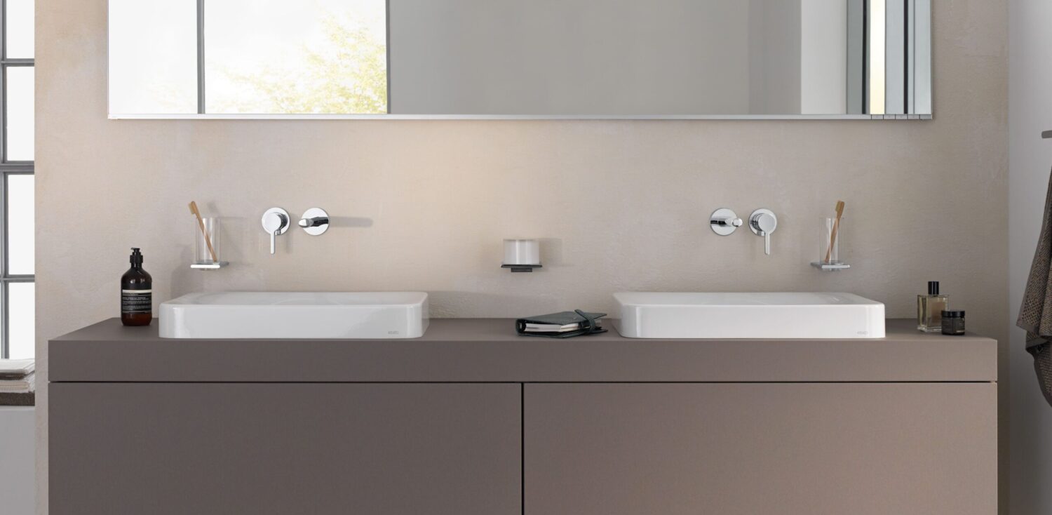 Modern bathroom with dual sinks, minimalistic design, and wall-mounted faucets. Toiletries and toothbrushes are neatly arranged, with a large mirror reflecting natural light.