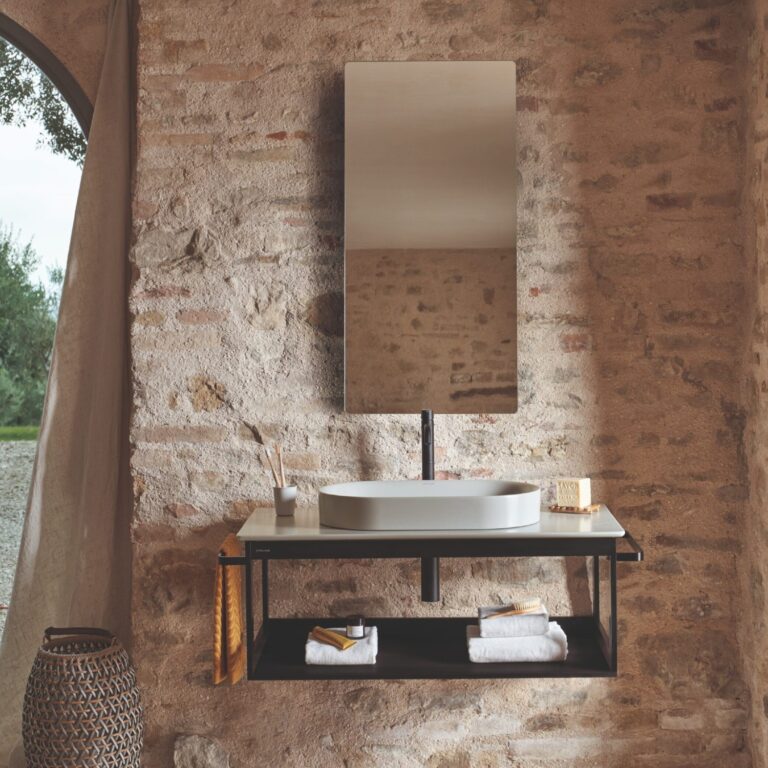 Modern bathroom with minimalist sink and mirror on a rustic brick wall. Natural light filters through an arched window, enhancing the serene atmosphere.