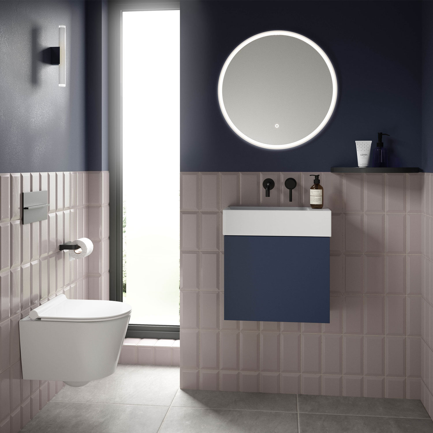 Modern bathroom with navy accents, round illuminated mirror, wall-mounted toilet, and compact sink. Minimalist design with light tiles and sleek fixtures.