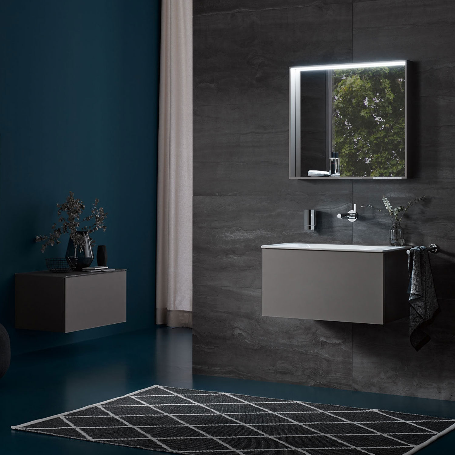 Modern bathroom with dark walls, floating vanity, and illuminated mirror. Minimalist design features greenery in a vase and geometric rug on the floor.