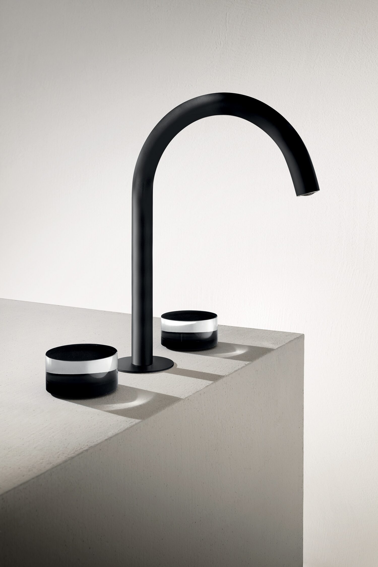 A sleek, modern black faucet with two matching handles is mounted on a light-colored countertop in a minimalist setting.