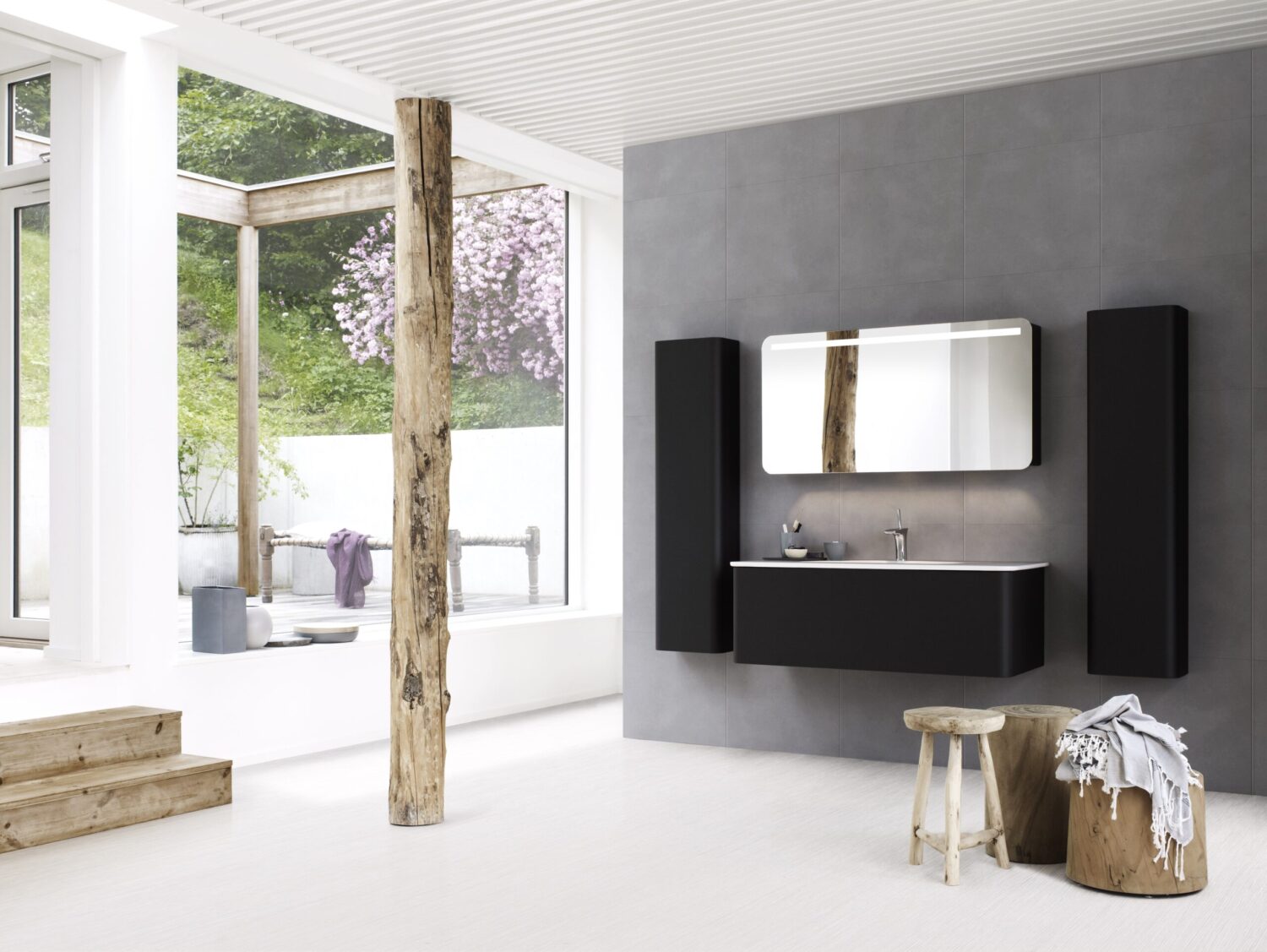 A modern bathroom with dark fixtures, wood elements, and large windows overlooking a serene garden with blossoming trees and natural light.