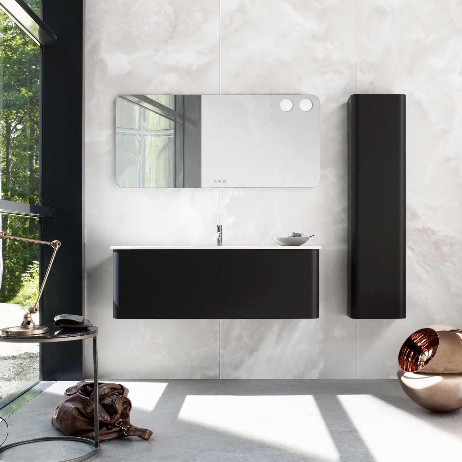 Minimalist bathroom with sleek black vanity, wall-mounted mirror, and modern lamp beside a window overlooking greenery. A bag rests on the floor.