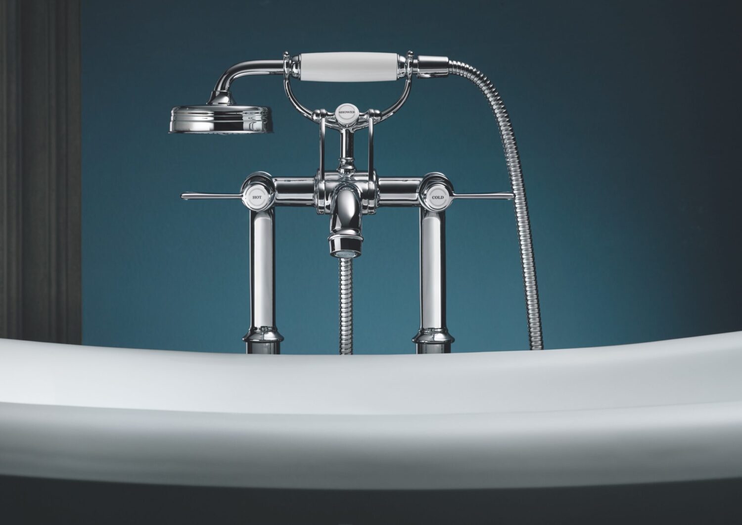 Close-up of a classic bathtub faucet with a handheld shower attachment against a dark teal wall, highlighting chrome details and retro design.