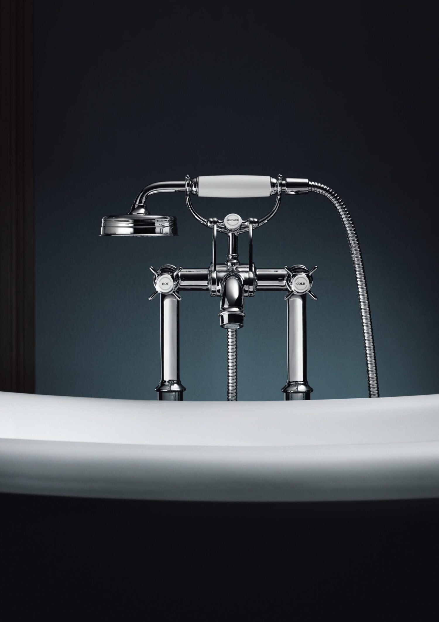 A close-up of a vintage-style chrome bathtub faucet with a handheld showerhead, set against a dark, minimalist background.