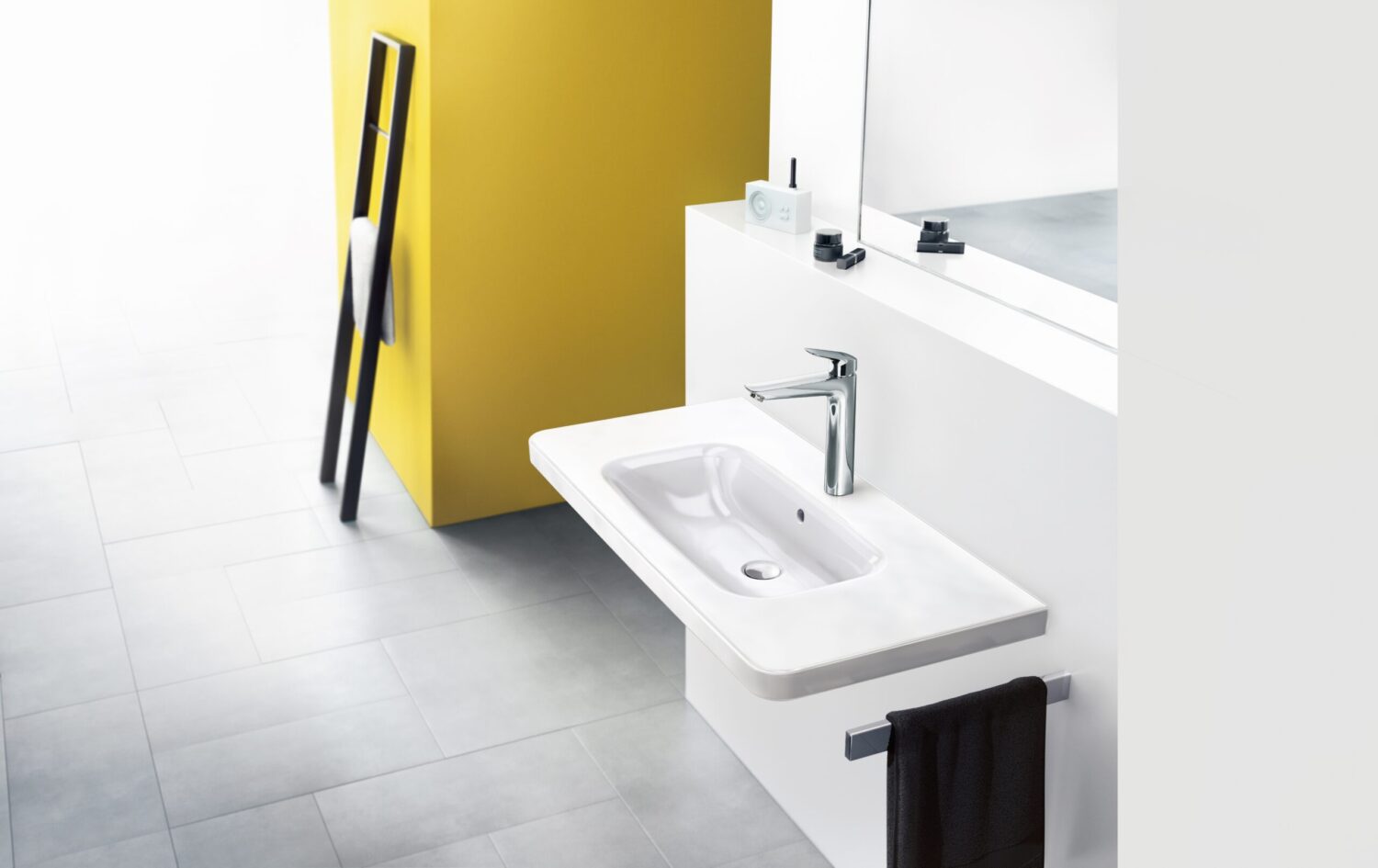 Modern bathroom with sleek white sink, chrome faucet, and large mirror. Yellow accent wall and black towel on ladder complete the minimalist decor.