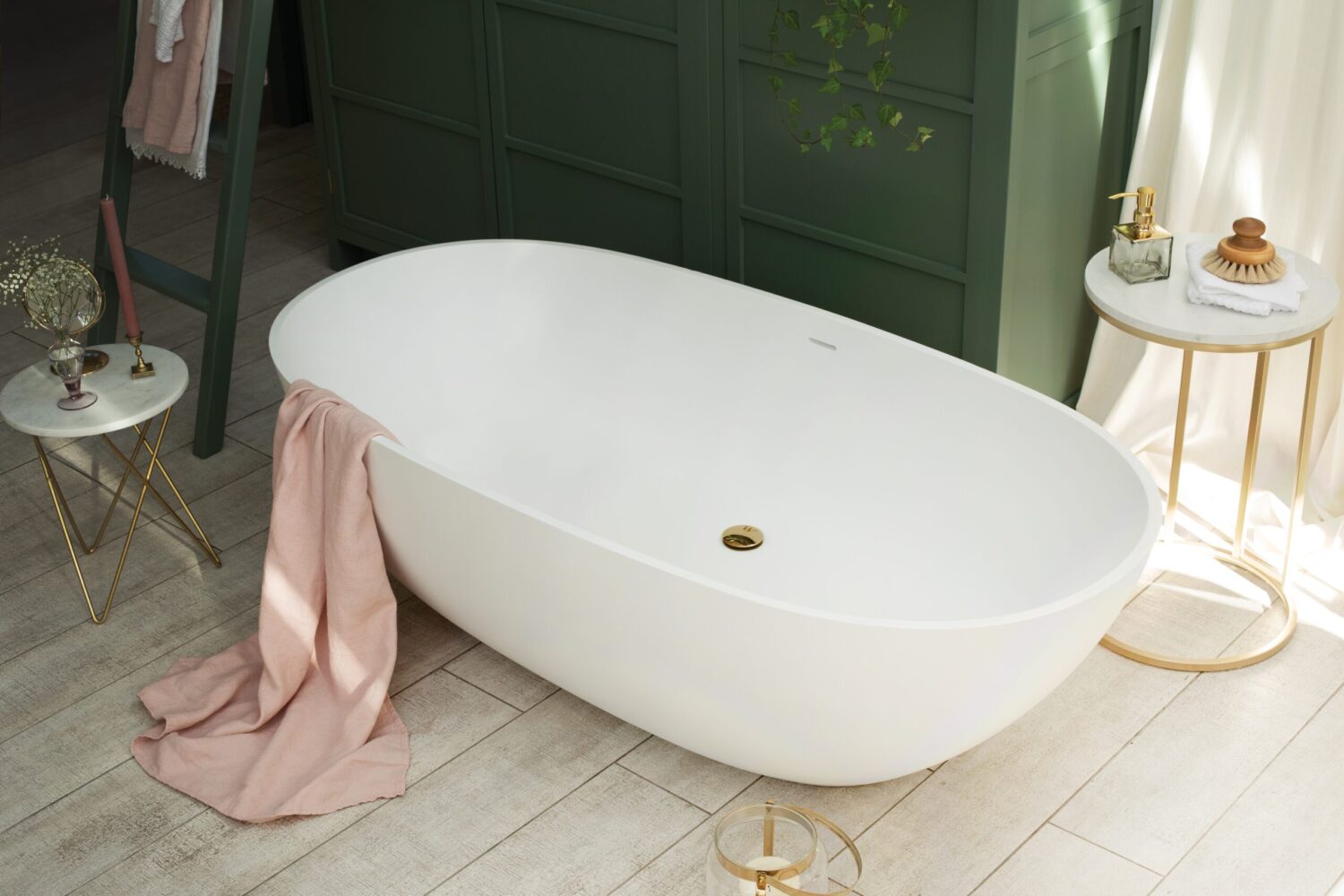 A white freestanding bathtub with a pink towel draped over it, surrounded by elegant decor and green paneling in a serene bathroom setting.