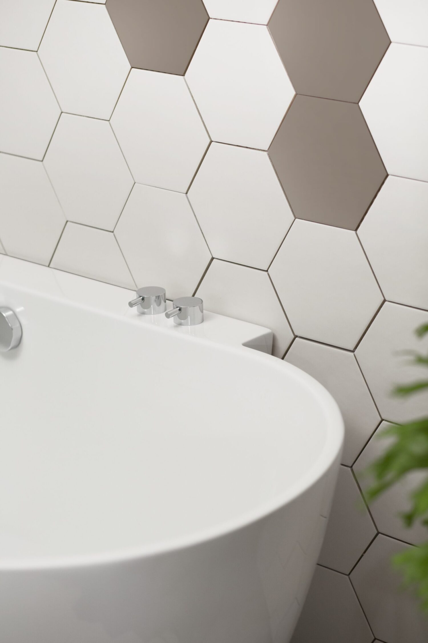 Modern bathroom features a white bathtub with sleek chrome fixtures, set against a geometric hexagon tile wall, and a potted plant nearby.