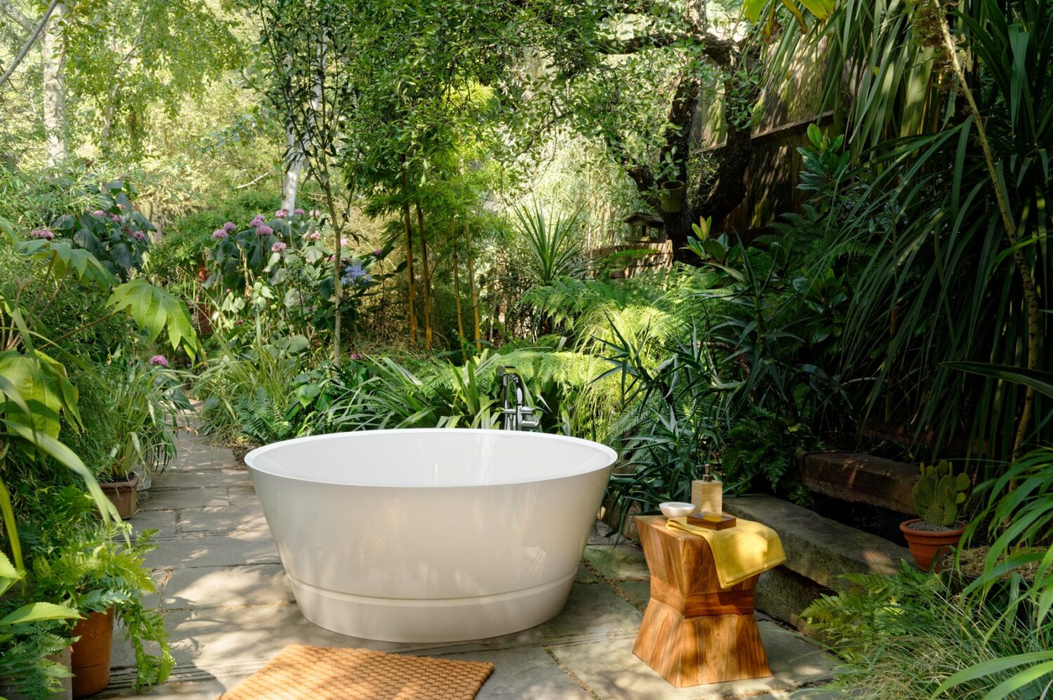 A serene outdoor bathtub surrounded by lush greenery and potted plants on a stone pathway, creating a tranquil, spa-like garden retreat.