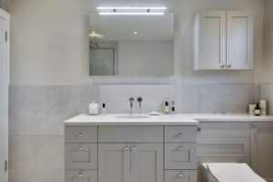 Modern bathroom with a large mirror, marble countertop, and light gray cabinets. Minimalist design with neatly arranged toiletries and soft lighting.