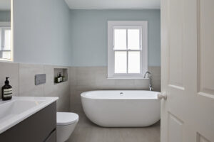 Contemporary bathroom featuring a freestanding bathtub, window, vanity, and modern fixtures. Minimalist design with neutral tones and clean lines throughout.