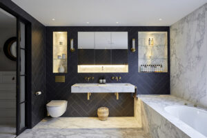 Luxurious modern bathroom with marble walls, freestanding bathtub, floating vanity, and backlit shelving. Dark herringbone tiles contrast with the white elements.