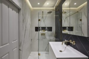 Modern bathroom with marble tiles, glass shower enclosure, and gold accents on fixtures. Large mirror reflects contemporary design. Elegant and minimalist appearance.