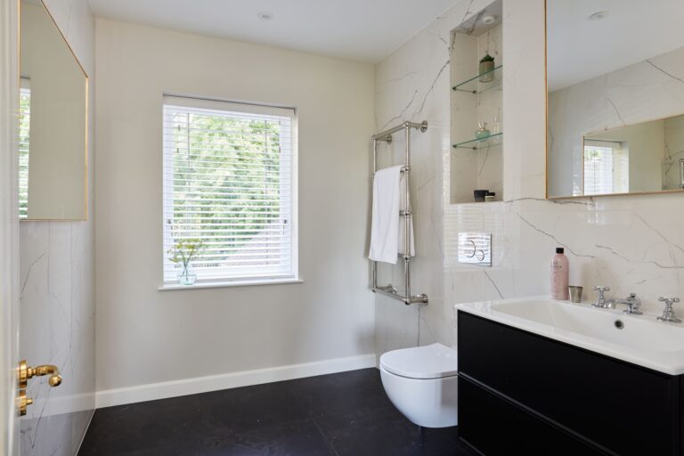 Modern bathroom with large window, black vanity, wall-mounted toilet, and towel rack. Light walls and marble-like tiles create a sleek, contemporary look.