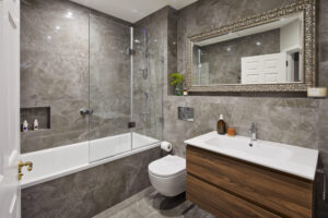 Modern bathroom with marble walls, glass shower door, wooden vanity, large decorative mirror, and white bathtub. Accessories include toiletries and a potted plant.