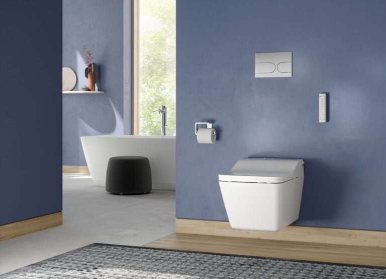 Modern bathroom with blue walls, featuring a white toilet, wall-mounted flush buttons, a sleek bathtub, black ottoman, and natural light.