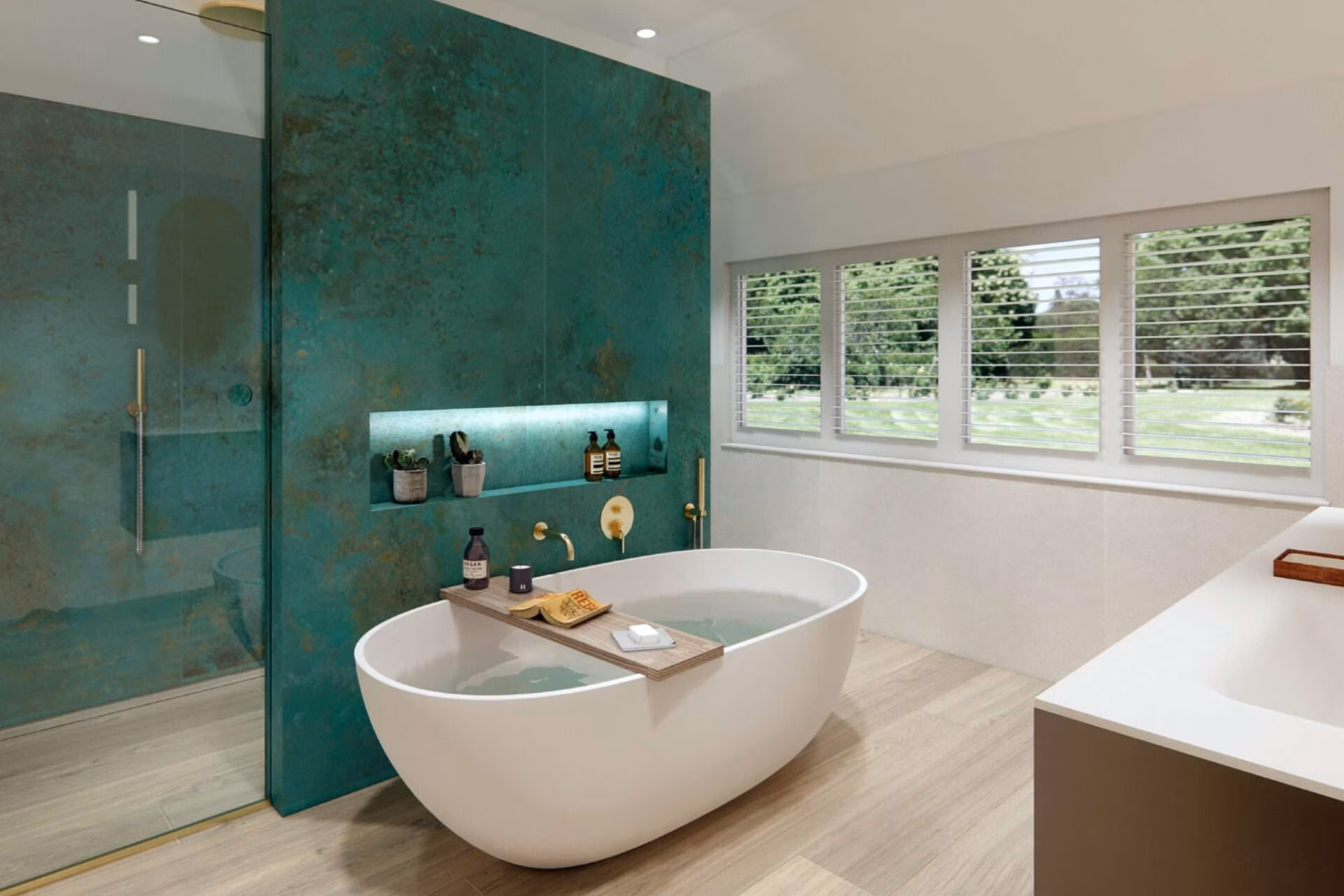 Modern bathroom features a freestanding bathtub, wooden floors, and teal walls. Large windows overlook a green garden, creating a serene atmosphere.