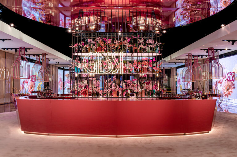 Modern interior with floral displays and "Gessi" signage. Redesigned space showcases vibrant colors, birdcage-style fixtures, and a sleek, contemporary bar area.