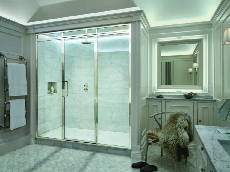 Luxurious bathroom with a marble shower, plush chair, and sleek vanity. Towel rack and slippers add comfort to the elegant design.