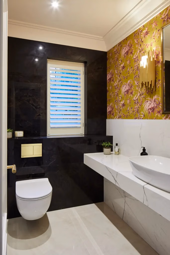 Elegant bathroom featuring a white sink, toilet, and decorative floral wallpaper with black and gold.