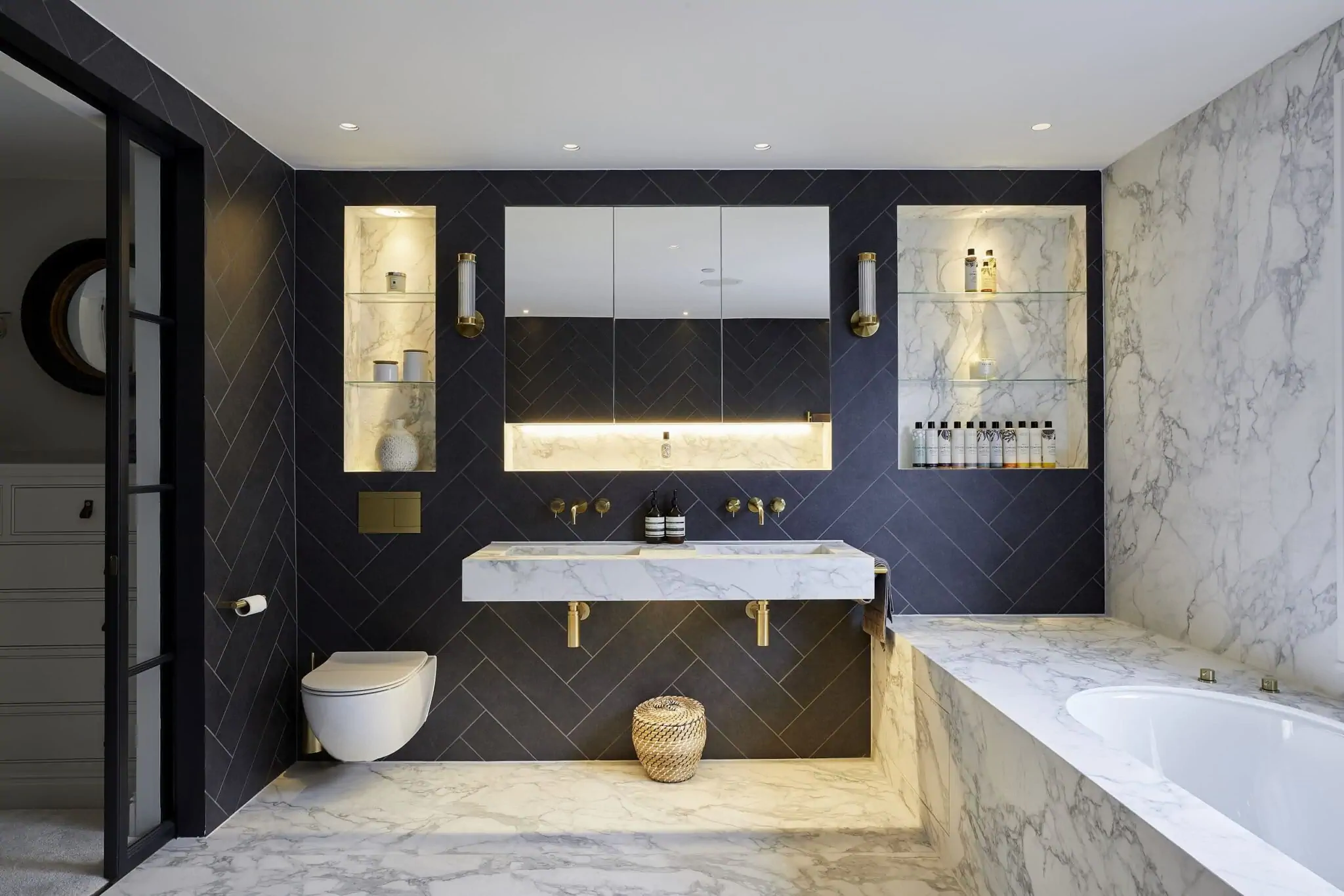 Modern bathroom with black and white marble design, floating sink, built-in shelves with lights, round bathtub, and minimalistic decor.