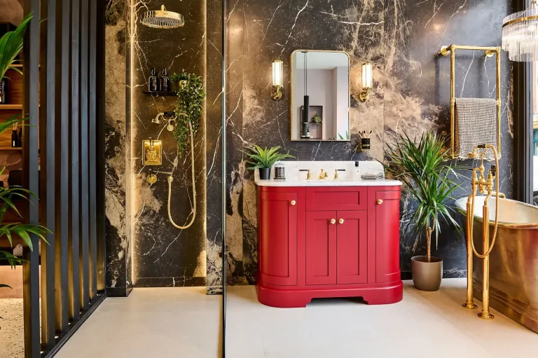 Elegant bathroom with red vanity, gold fixtures, marble walls, and lush greenery.