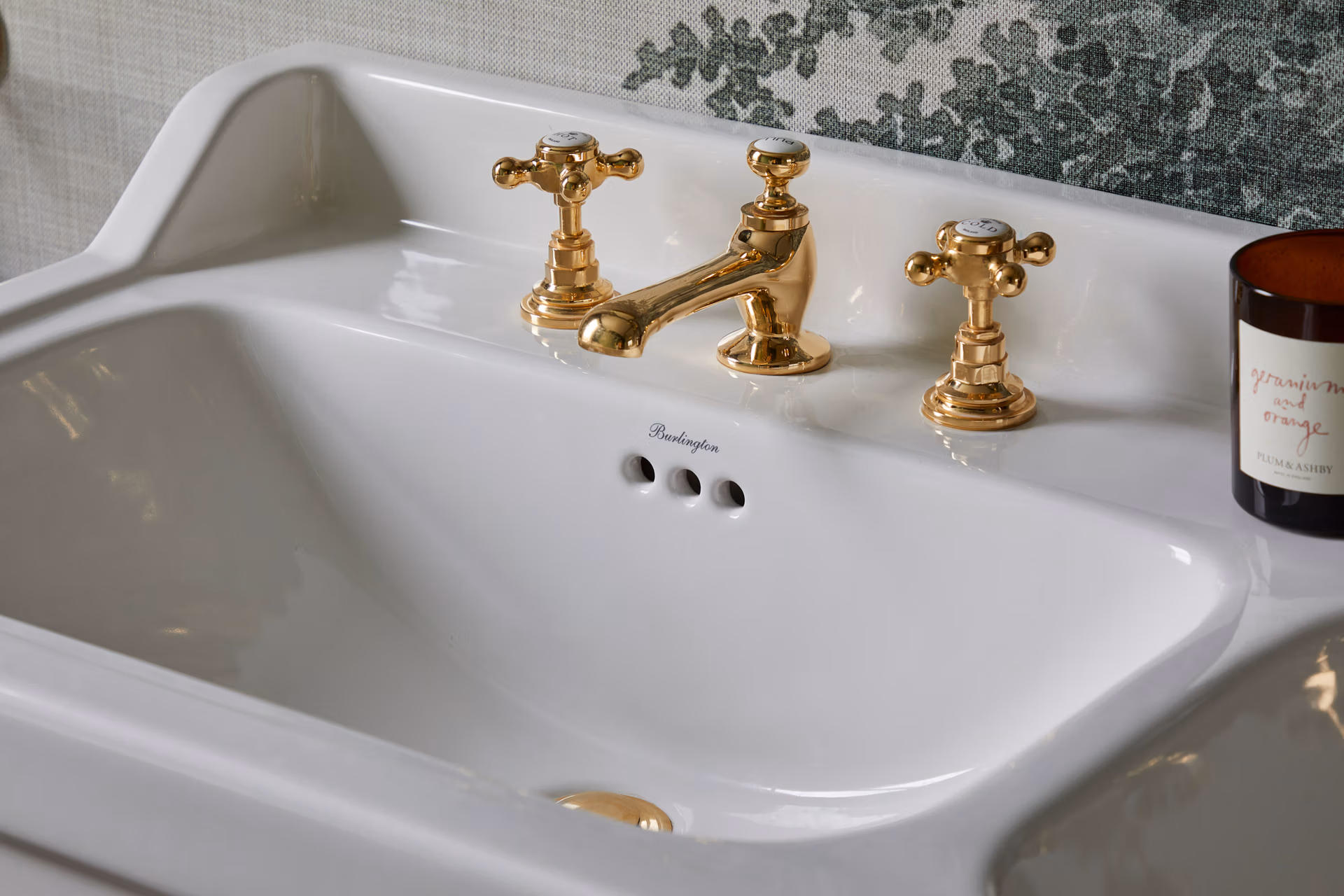 A bathroom sink featuring elegant gold faucets and a lit candle, creating a warm and inviting atmosphere.