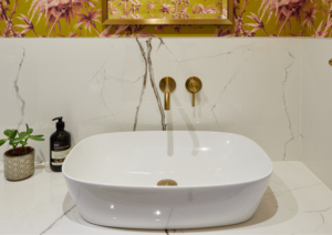 Elegant bathroom sink with gold tap fittings and marble wall background.