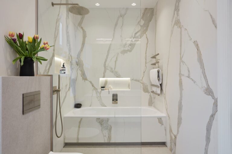 Luxurious bathroom with white marble walls, featuring a bathtub and glass shower. Tulips in a vase add color, while soft lighting creates a serene ambiance.