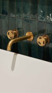 Close-up of vintage brass bathroom tap and wall-mounted fixtures with green tiles.
