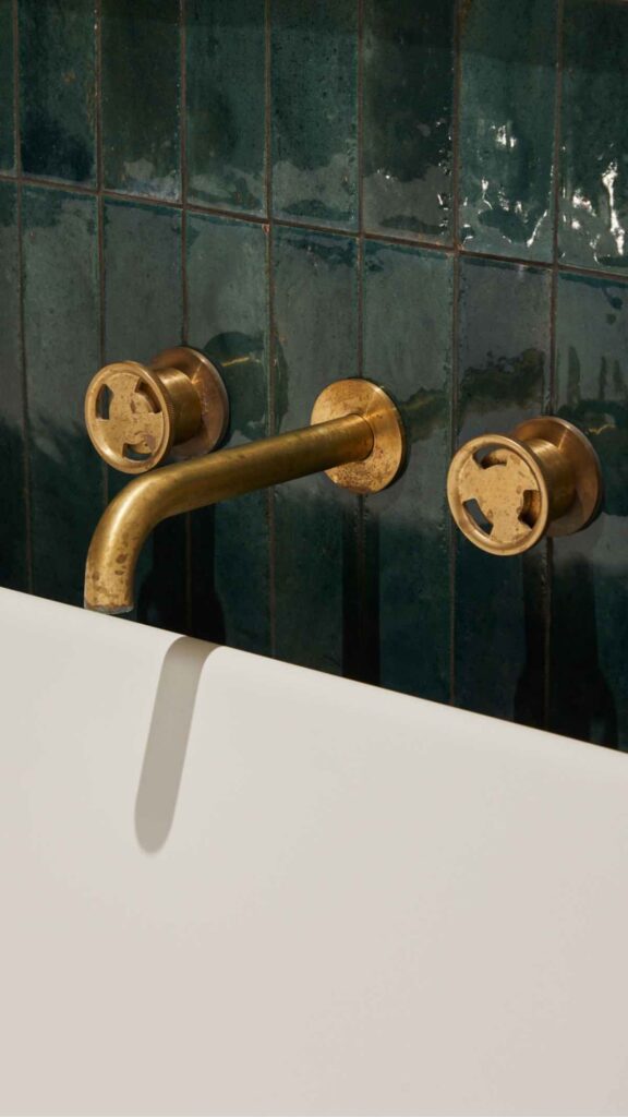 Close-up of vintage brass bathroom tap and wall-mounted fixtures with green tiles.
