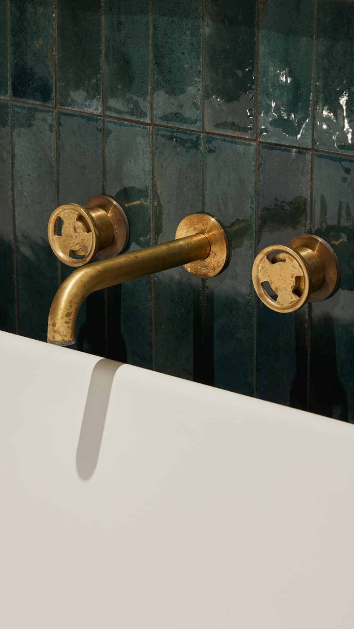 Close-up of vintage brass bathroom tap and wall-mounted fixtures with green tiles.