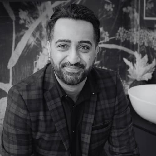 Professional man in a checkered blazer smiling in a modern bathroom setting.